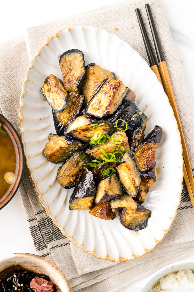 A white oval ceramic plate containing stir fry miso eggplant garnished with scallion.