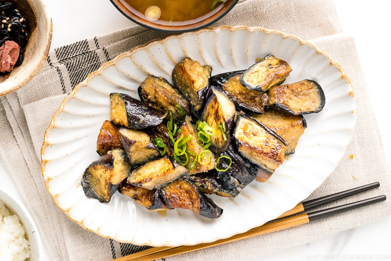 A white oval ceramic plate containing stir fry miso eggplant garnished with scallion.