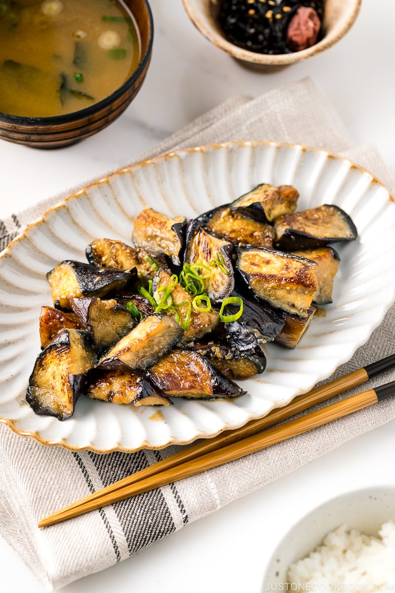 A white oval ceramic plate containing stir fry miso eggplant garnished with scallion.