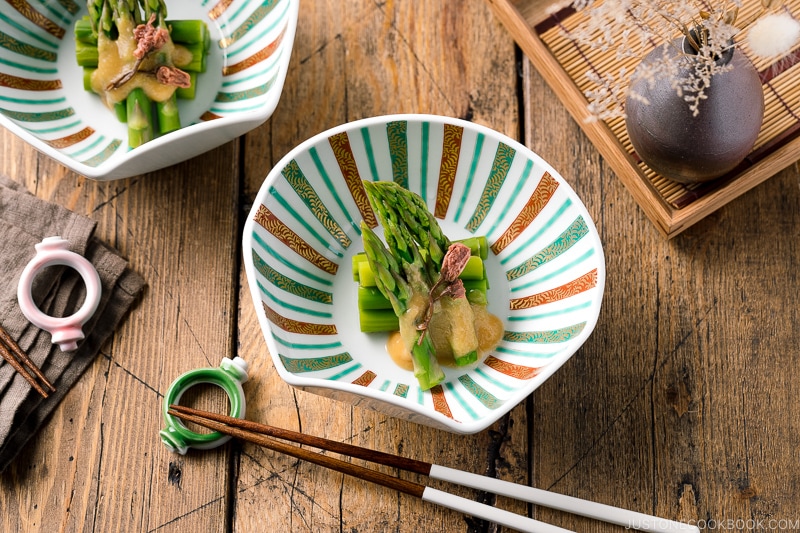 A shell shaped bowl containing Asparagus with Miso Dressing (Karashi Sumisoae) garnished with salt pickled cherry blossom.