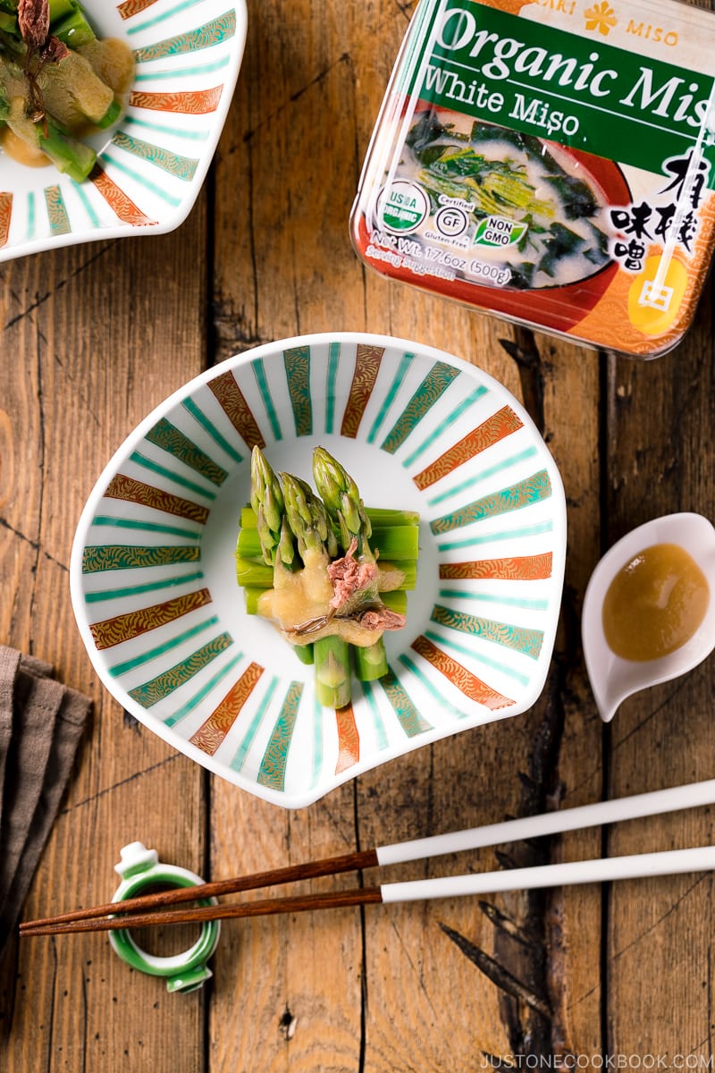 A shell shaped bowl containing Asparagus with Miso Dressing (Karashi Sumisoae) garnished with salt pickled cherry blossom.