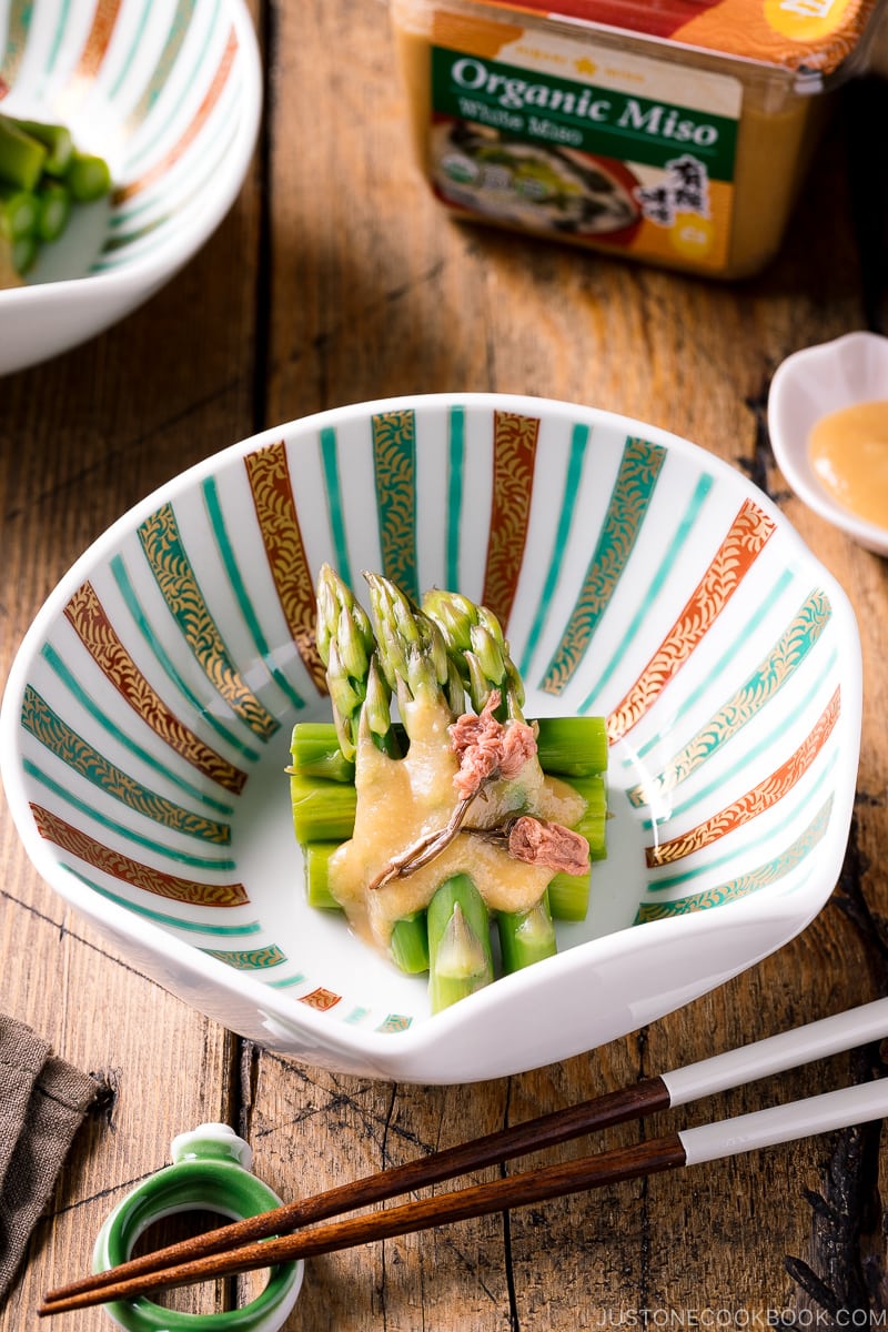 A shell shaped bowl containing Asparagus with Miso Dressing (Karashi Sumisoae) garnished with salt pickled cherry blossom.