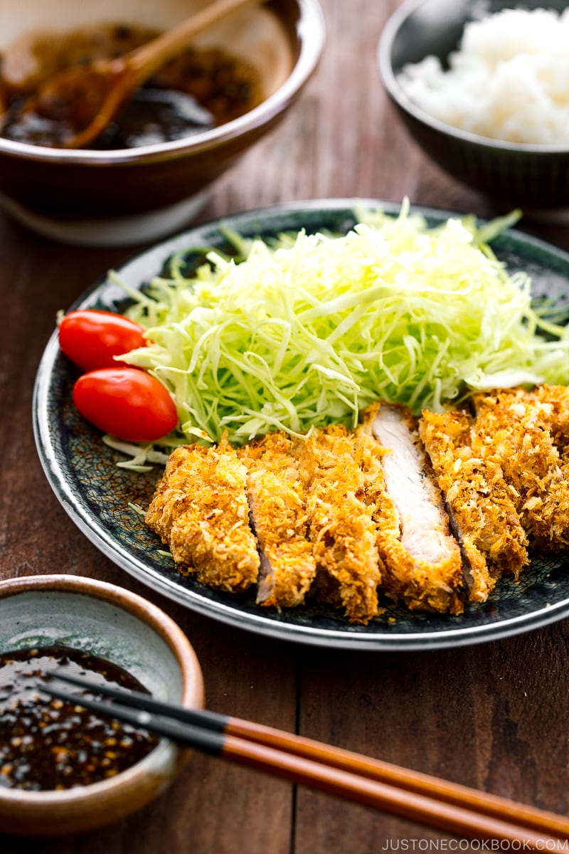 A plate containing baked tonkatsu, shredded cabbage, and cherry tomatoes.