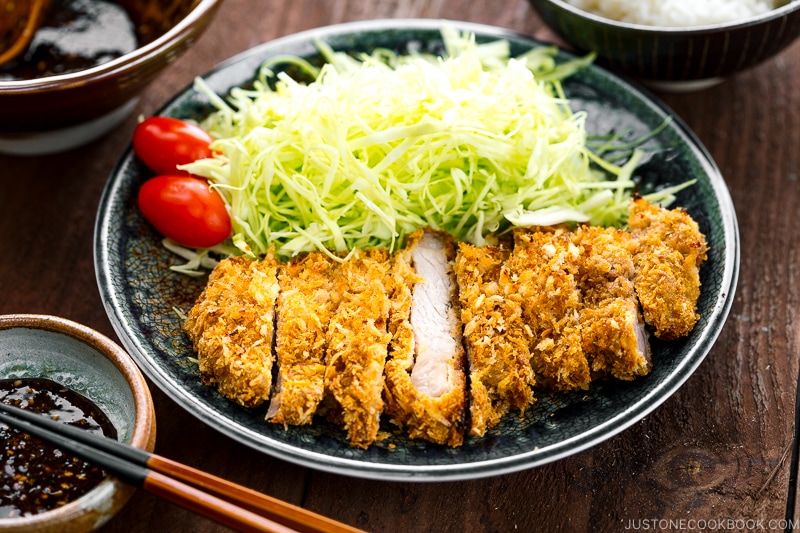 A plate containing baked tonkatsu, shredded cabbage, and cherry tomatoes.