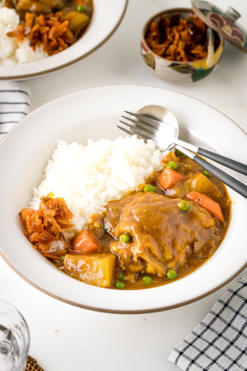 A white ceramic bowl containing steamed rice and Japanese bone-in chicken curry garnished with fukujinzuke.