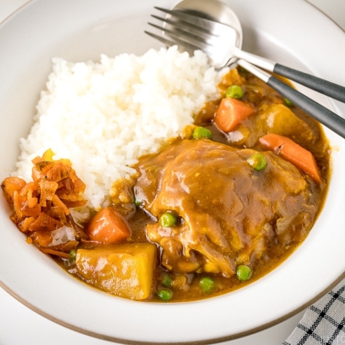 A white ceramic bowl containing steamed rice and Japanese bone-in chicken curry garnished with fukujinzuke.