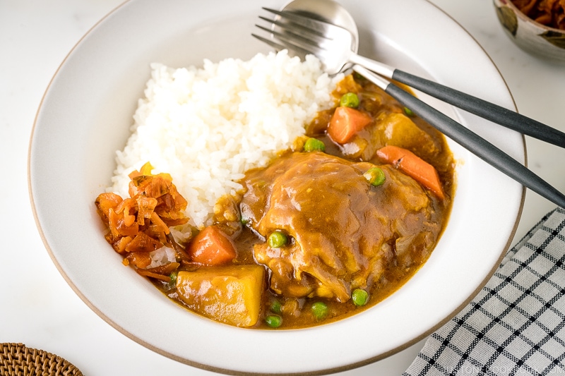 A white ceramic bowl containing steamed rice and Japanese bone-in chicken curry garnished with fukujinzuke.