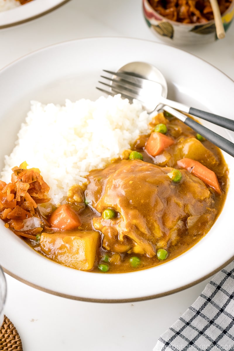 A white ceramic bowl containing steamed rice and Japanese bone-in chicken curry garnished with fukujinzuke.