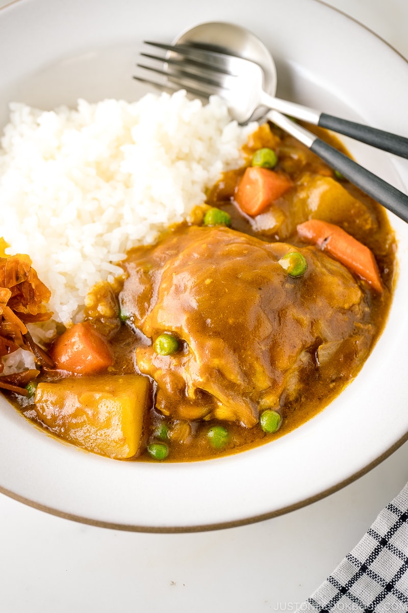 A white ceramic bowl containing steamed rice and Japanese bone-in chicken curry garnished with fukujinzuke.