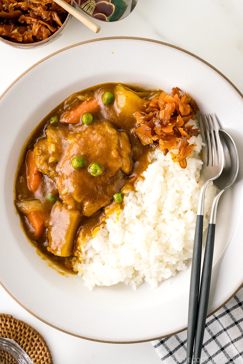 A white ceramic bowl containing steamed rice and Japanese bone-in chicken curry garnished with fukujinzuke.