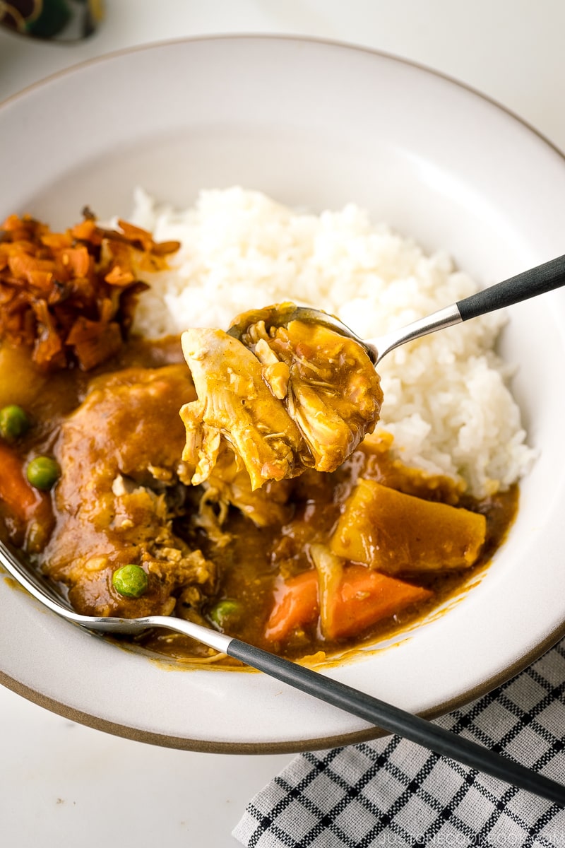 A white ceramic bowl containing steamed rice and Japanese bone-in chicken curry garnished with fukujinzuke.