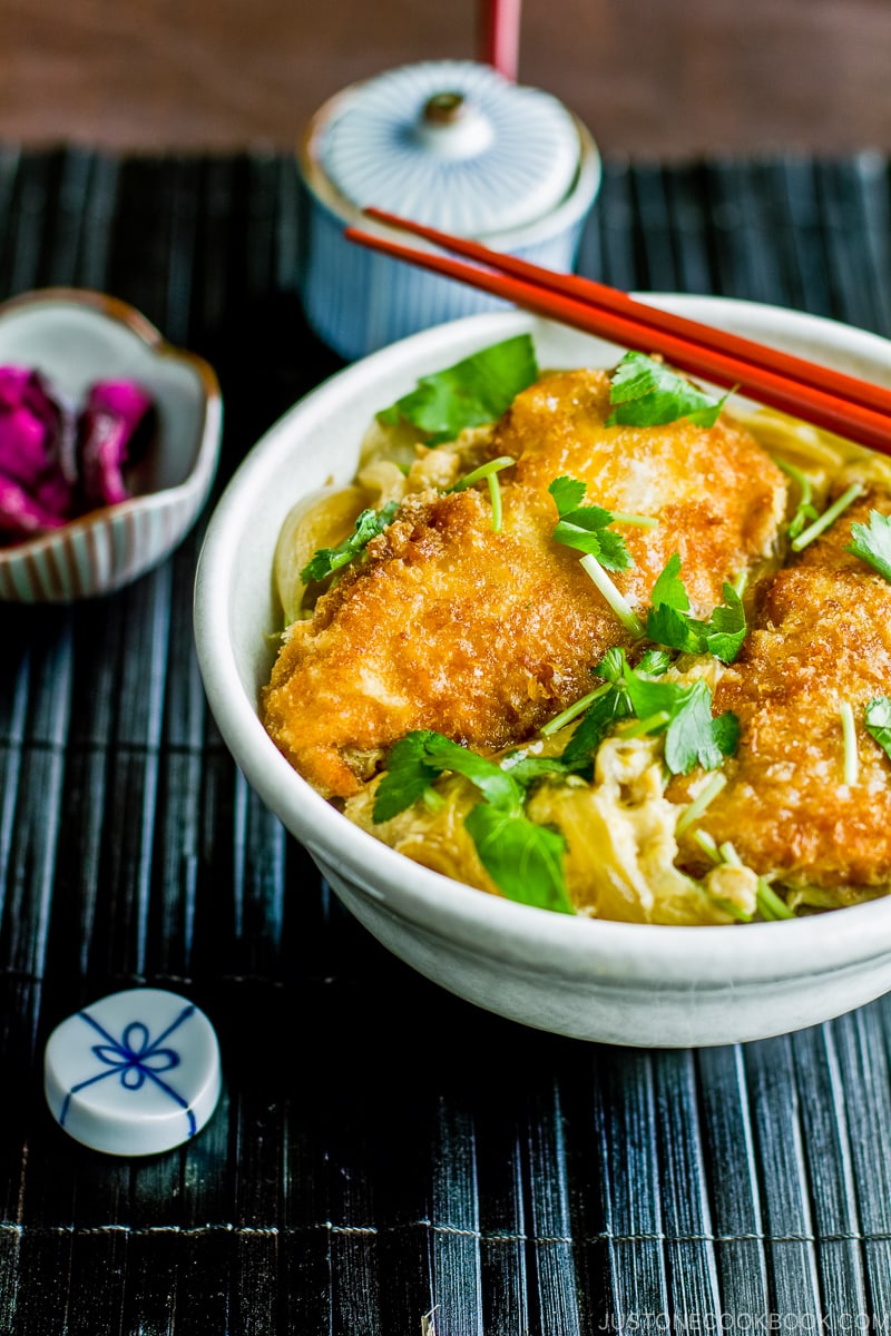 A white large donburi bowl containing steamed rice topped with chicken katsu, egg, and onion cooked in the savory seasoning.