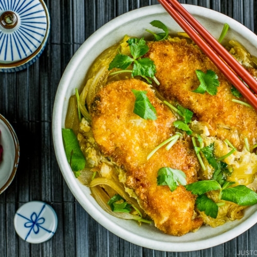 A white large donburi bowl containing steamed rice topped with chicken katsu, egg, and onion cooked in the savory seasoning.