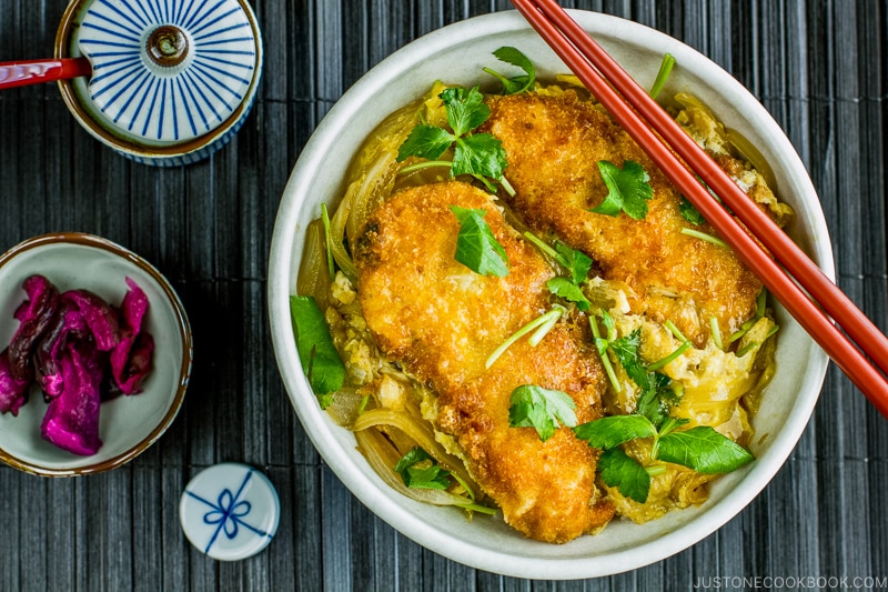 A white large donburi bowl containing steamed rice topped with chicken katsu, egg, and onion cooked in the savory seasoning.