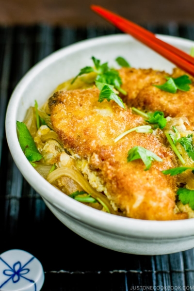 A white large donburi bowl containing steamed rice topped with chicken katsu, egg, and onion cooked in the savory seasoning.