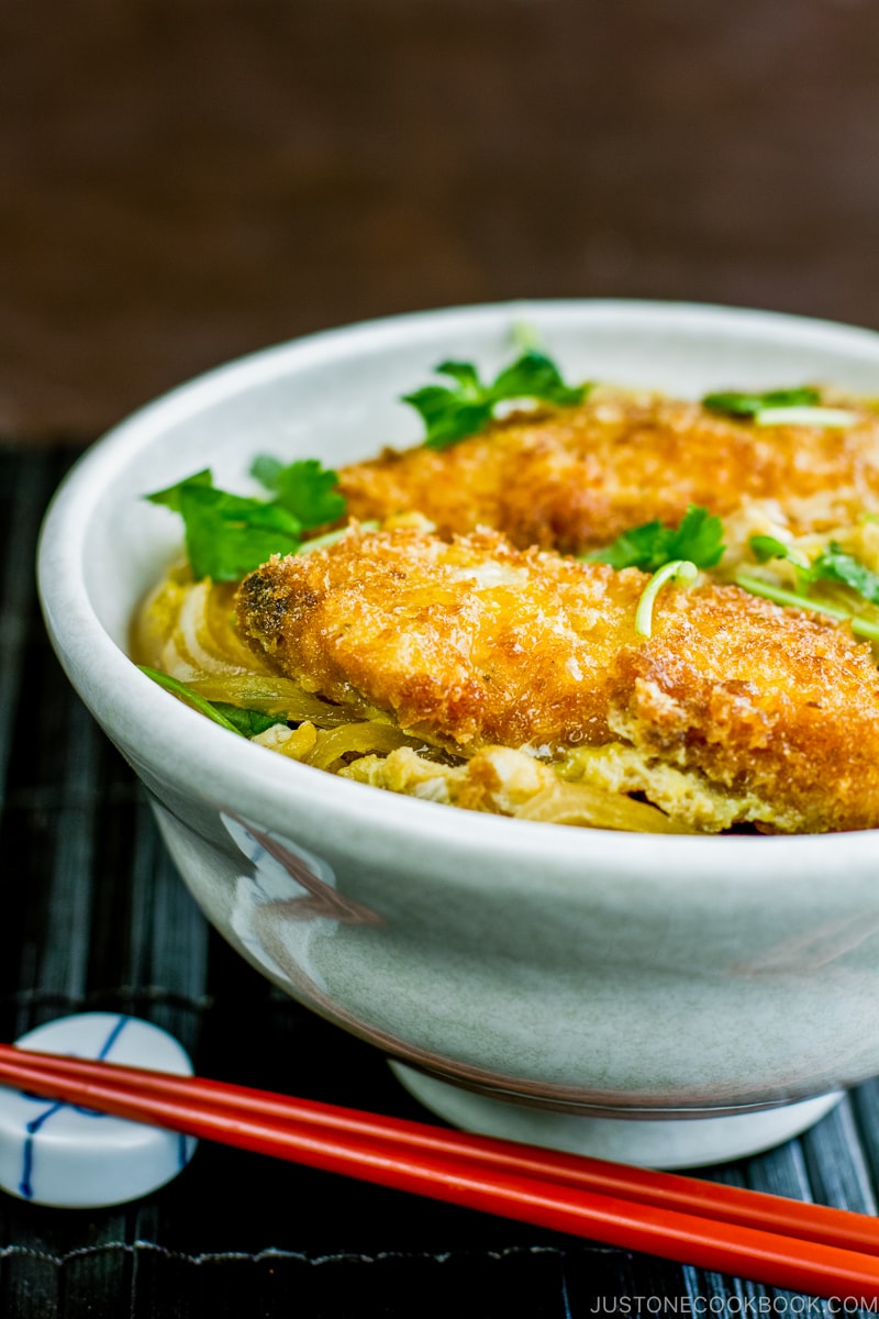 A white large donburi bowl containing steamed rice topped with chicken katsu, egg, and onion cooked in the savory seasoning.