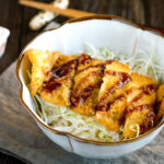 A donburi bowl containing crispy tonkatsu over rice topped with tonkatsu sauce.