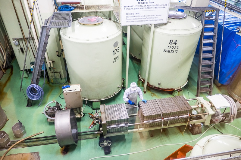 workers working in sake brewery next to large vats