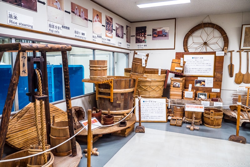 historical sake making tools on display along the wall including various size vats