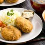 A plate containing menchi katsu (ground meat cutlet) along with shredded vegetables and tartar sauce.