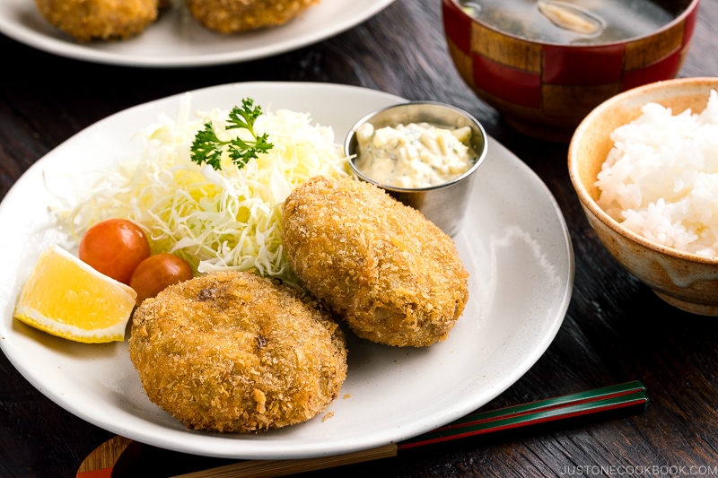 A plate containing menchi katsu (ground meat cutlet) along with shredded vegetables and tartar sauce.