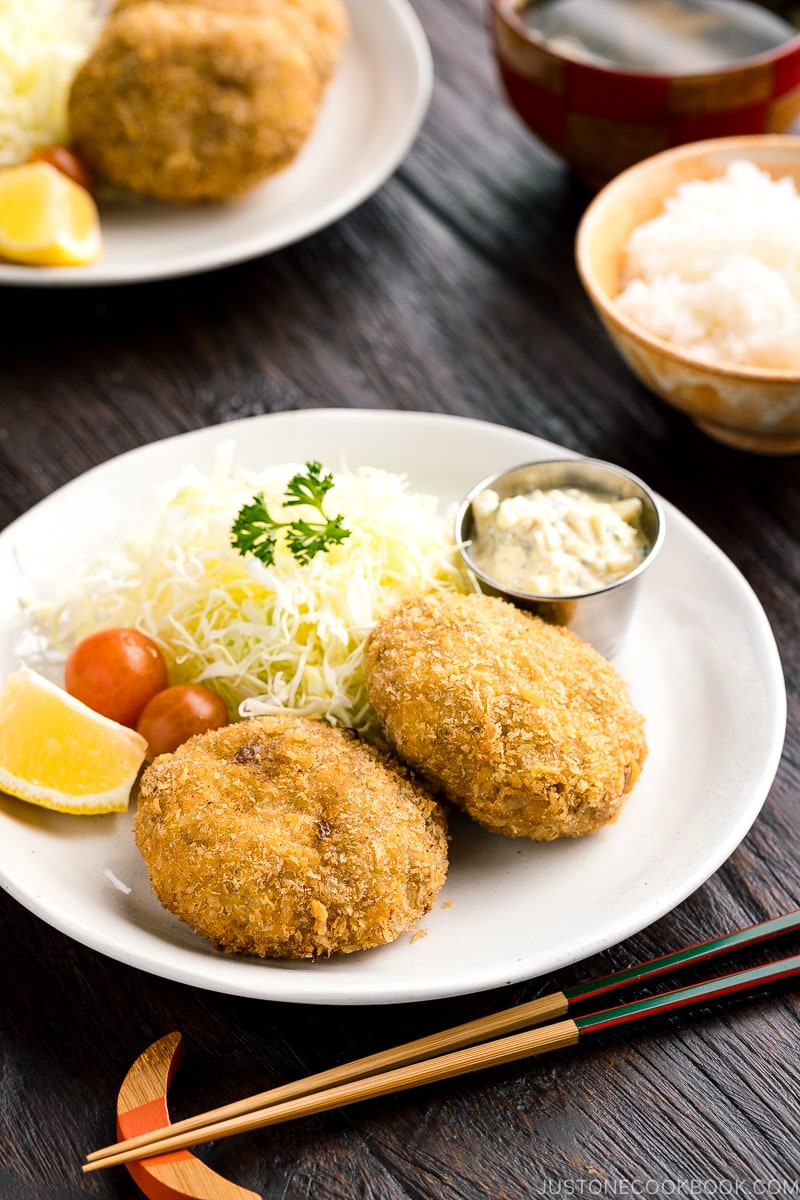 A plate containing menchi katsu (ground meat cutlet) along with shredded vegetables and tartar sauce.