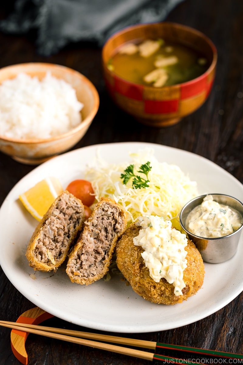 A plate containing menchi katsu (ground meat cutlet) along with shredded vegetables and tartar sauce.