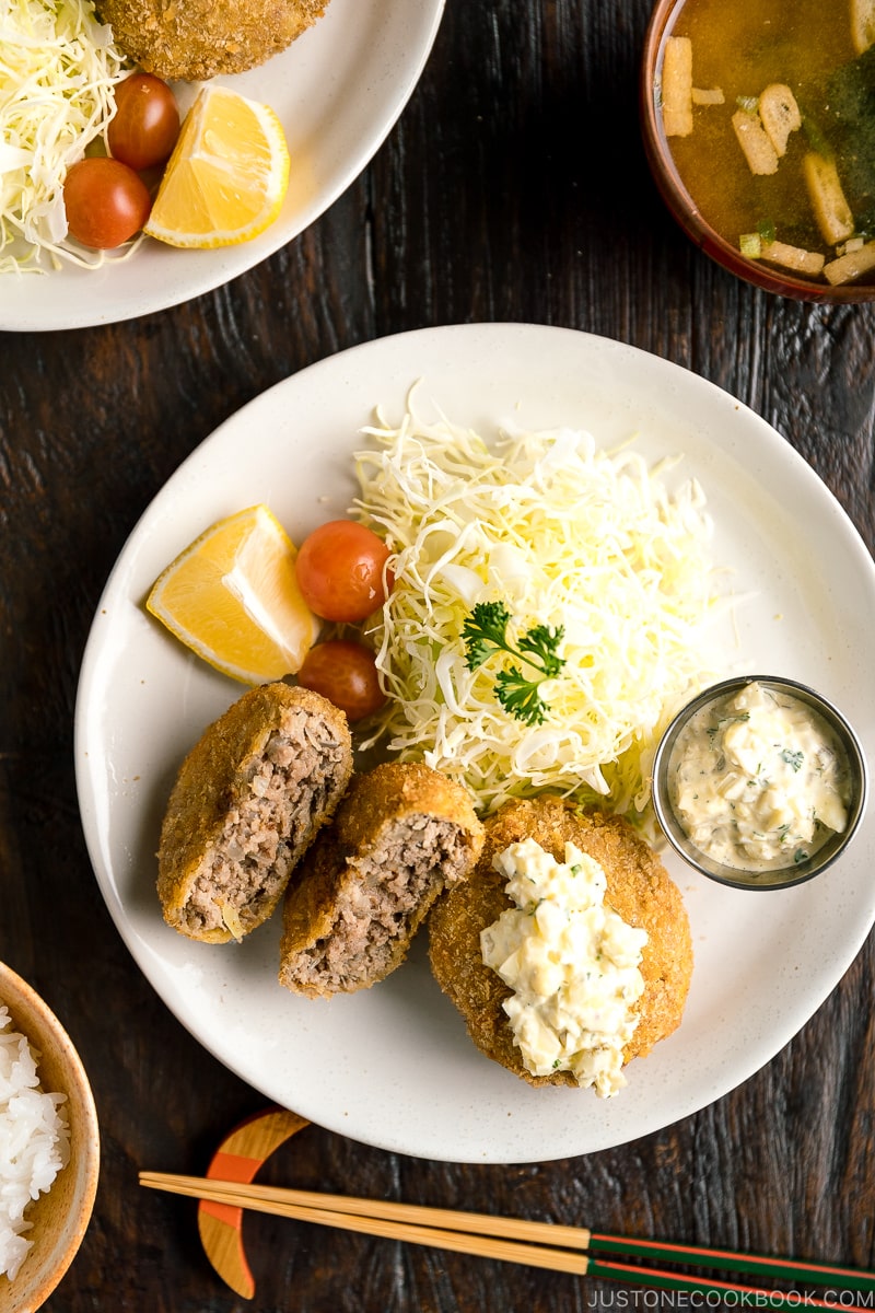A plate containing menchi katsu (ground meat cutlet) along with shredded vegetables and tartar sauce.