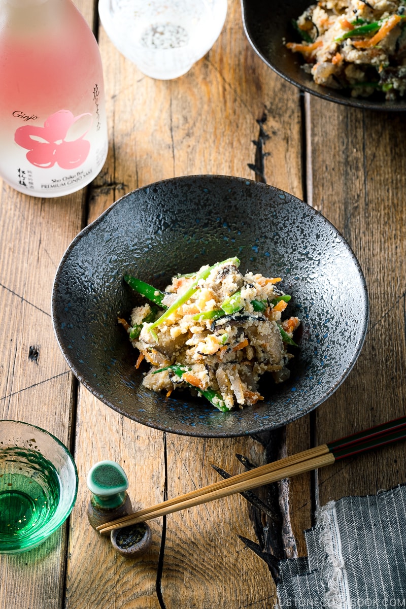 A black bowl containing Okara (Unohana) mixed with assorted vegetables, shiitake mushroom, seaweed, and konnyaku.