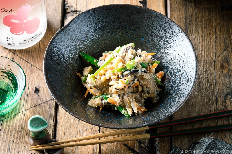 A black bowl containing Okara (Unohana) mixed with assorted vegetables, shiitake mushroom, seaweed, and konnyaku.