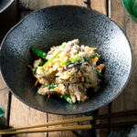 A black bowl containing Okara (Unohana) mixed with assorted vegetables, shiitake mushroom, seaweed, and konnyaku.