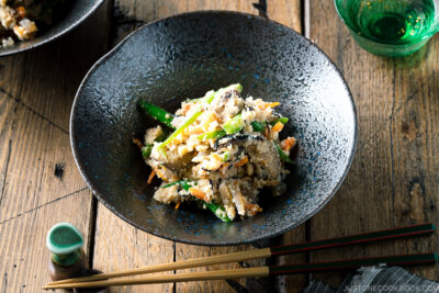 A black bowl containing Okara (Unohana) mixed with assorted vegetables, shiitake mushroom, seaweed, and konnyaku.