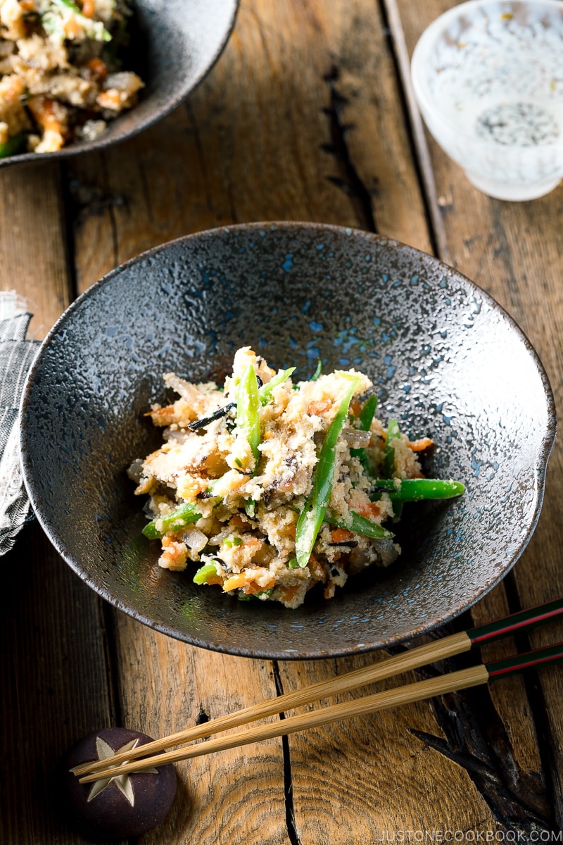 A black bowl containing Okara (Unohana) mixed with assorted vegetables, shiitake mushroom, seaweed, and konnyaku.