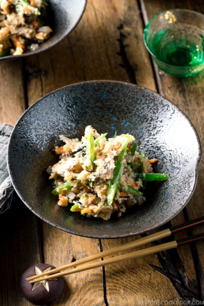 A black bowl containing Okara (Unohana) mixed with assorted vegetables, shiitake mushroom, seaweed, and konnyaku.