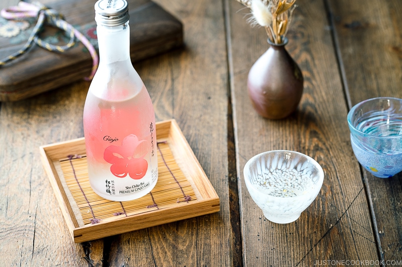 Sho Chiku Bai Ginjo Sake bottle on a wood tray next to sake glass and a vase on top of wood table
