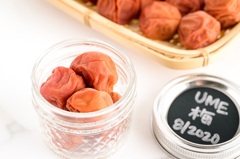 A glass jar and a bamboo strainer containing umeboshi (Japanese pickled plums).