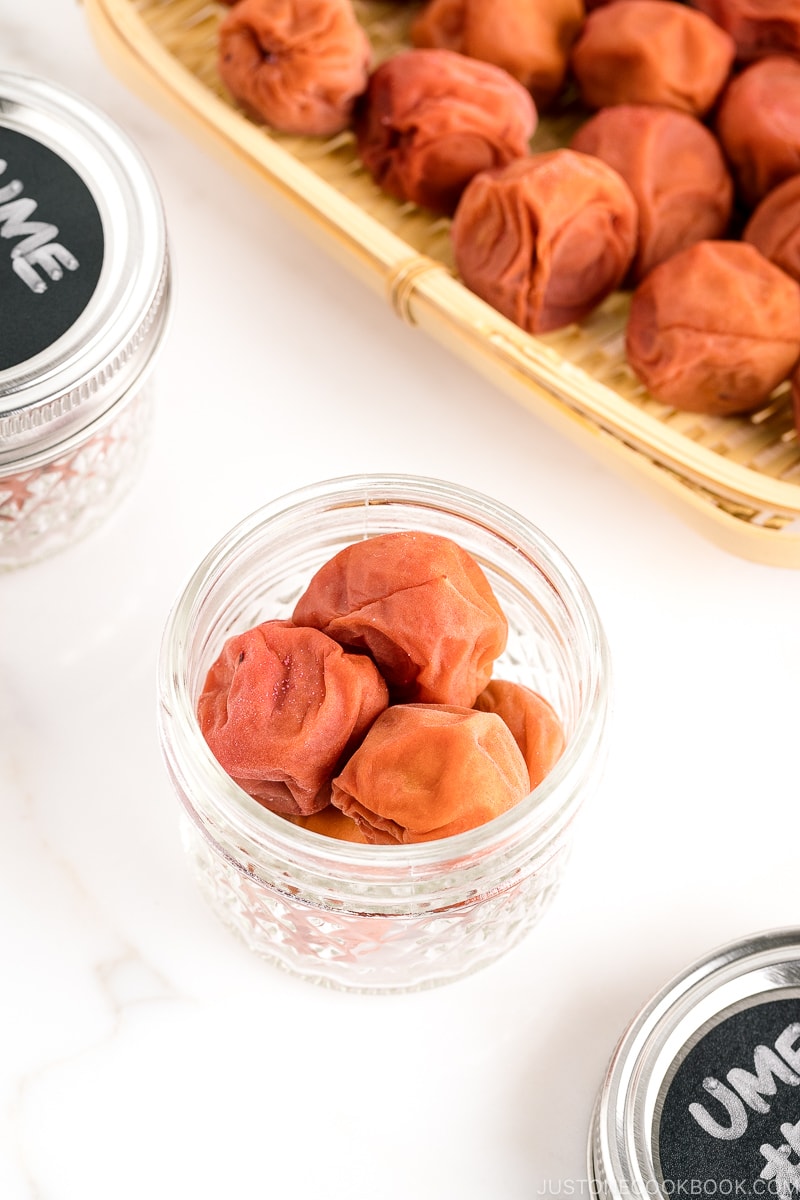 A glass jar and a bamboo strainer containing umeboshi (Japanese pickled plums).