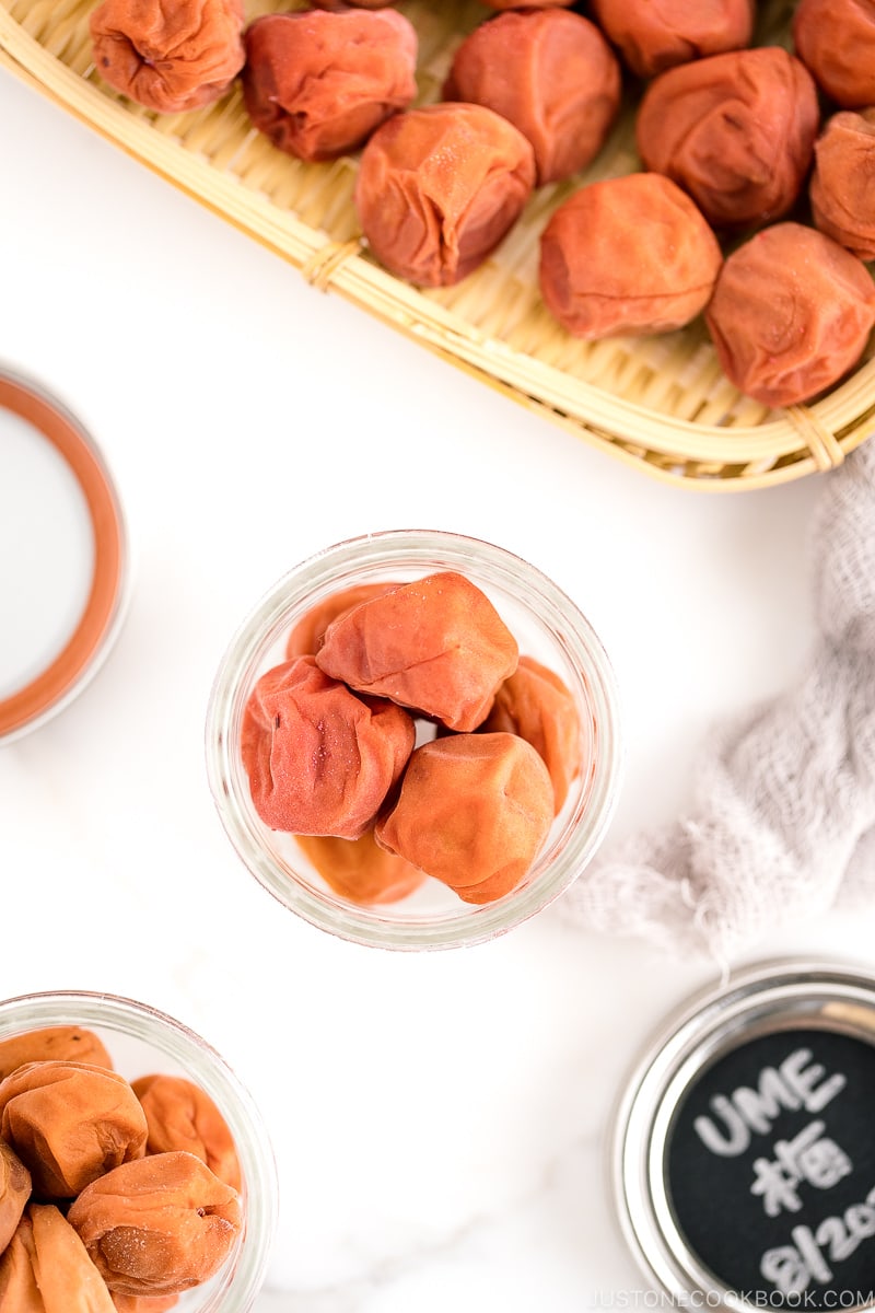 A glass jar and a bamboo strainer containing umeboshi (Japanese pickled plums).