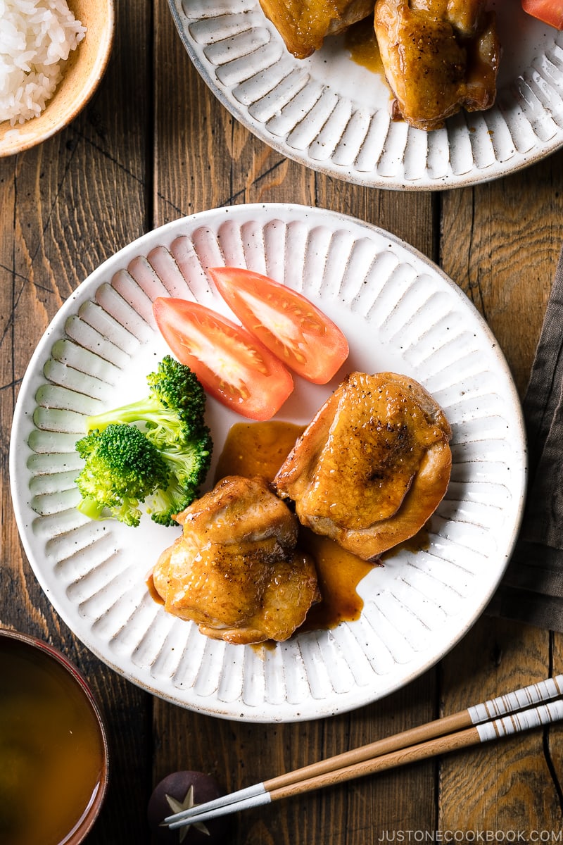 A plate containing butter shoyu chicken, broccoli, and tomatoes.