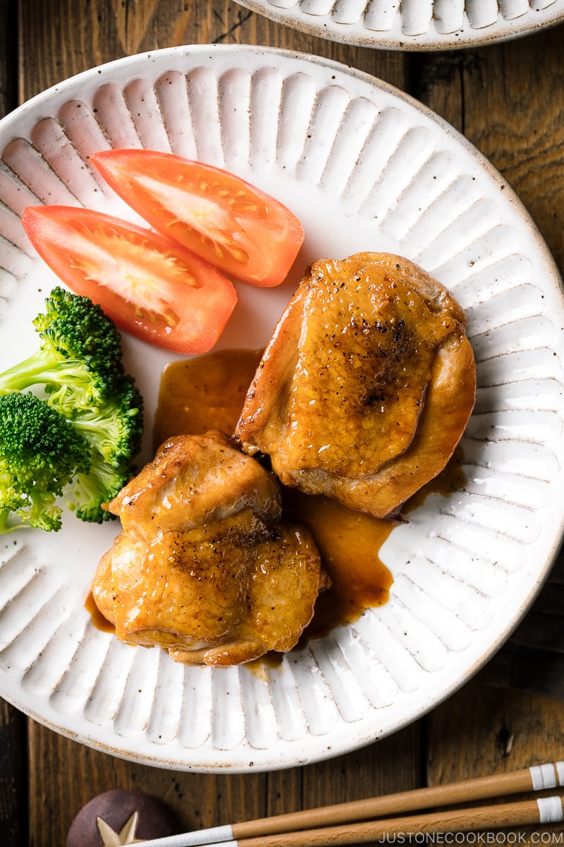 A plate containing butter shoyu chicken, broccoli, and tomatoes.