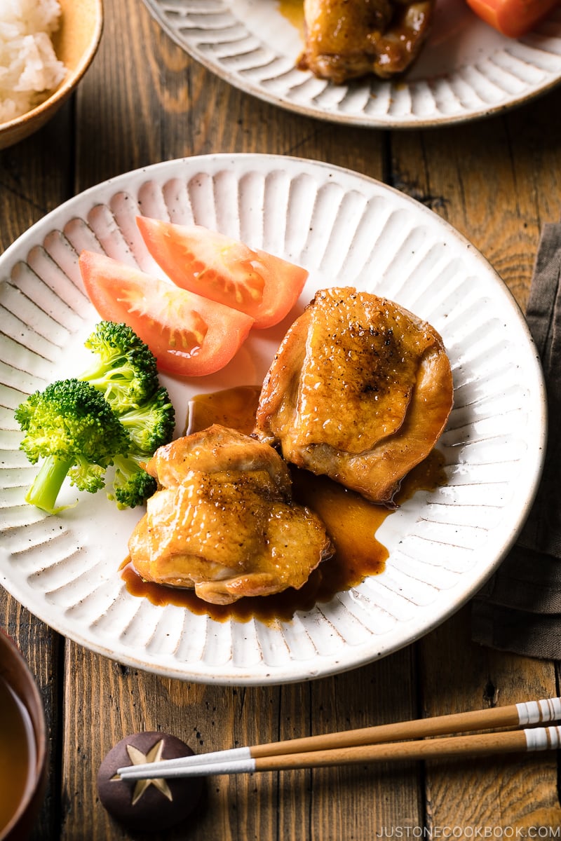 A plate containing butter shoyu chicken, broccoli, and tomatoes.