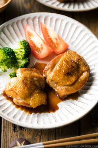 A plate containing butter shoyu chicken, broccoli, and tomatoes.