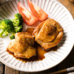 A plate containing butter shoyu chicken, broccoli, and tomatoes.