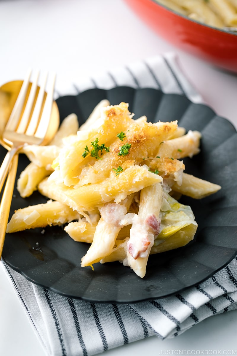 A black plate containing creamy napa cabbage and bacon pasta.