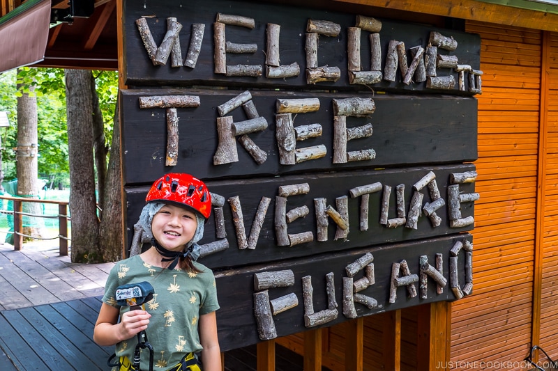 a girl in front of Tree Adventure Furano sign