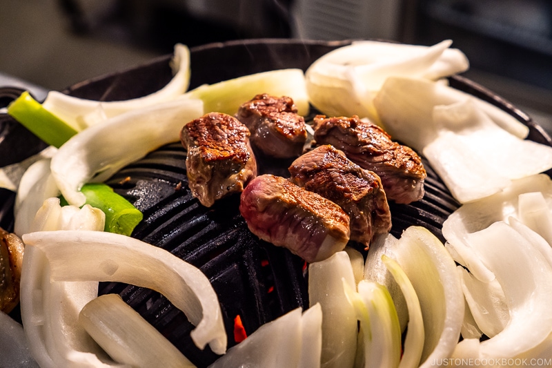lamb and onions grilling on a metal grate