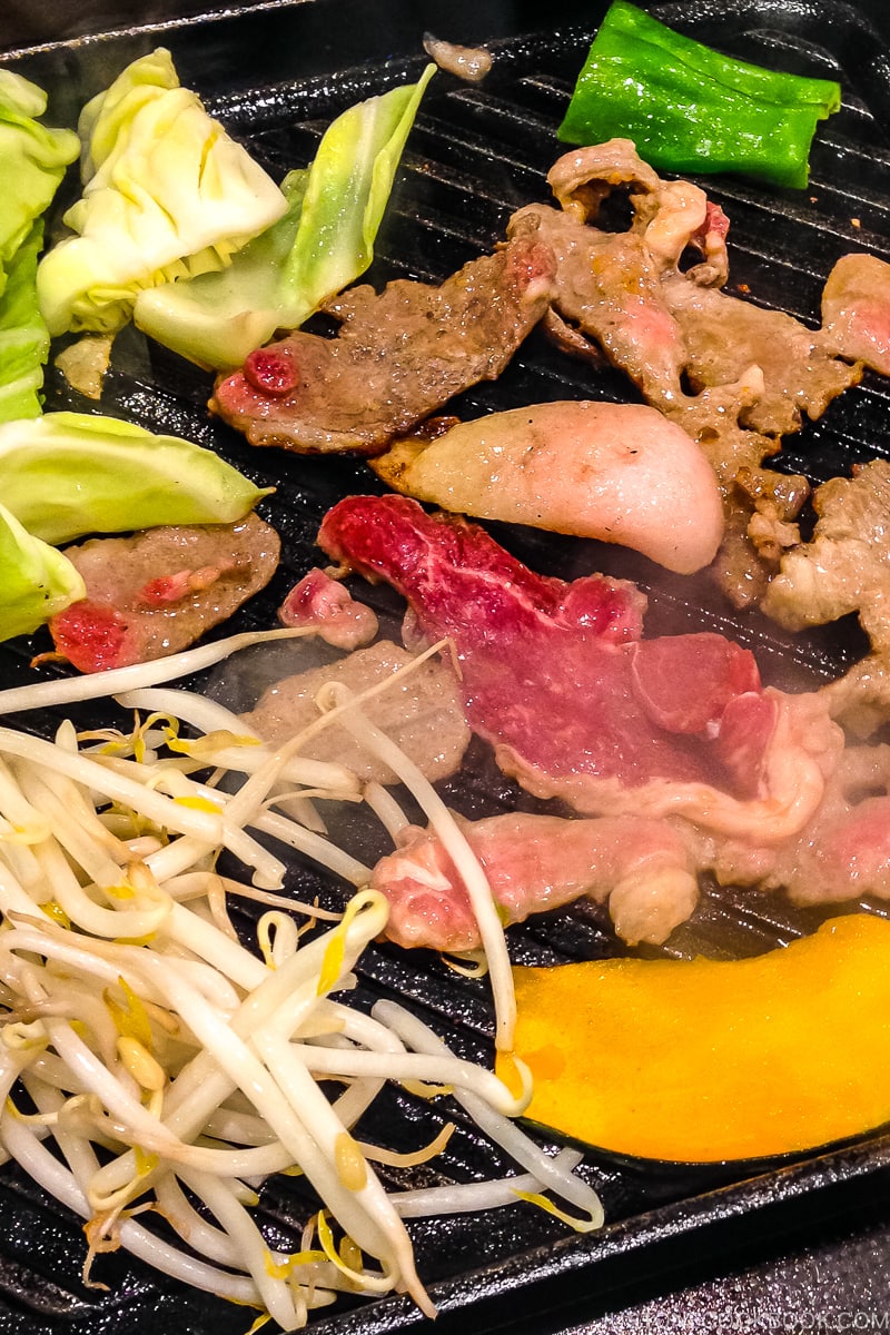 lamb, cabbage, kabocha, and bean sprout grilling on a metal grate