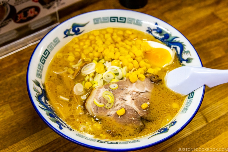 a bowl of ramen with corn and chasu on wood table