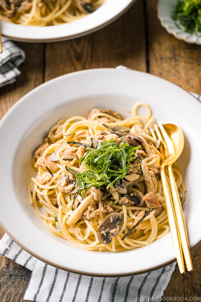 A white ceramic plate containing Japanese-style Tuna Mushroom Pasta garnished with shredded nori and shiso leaves.