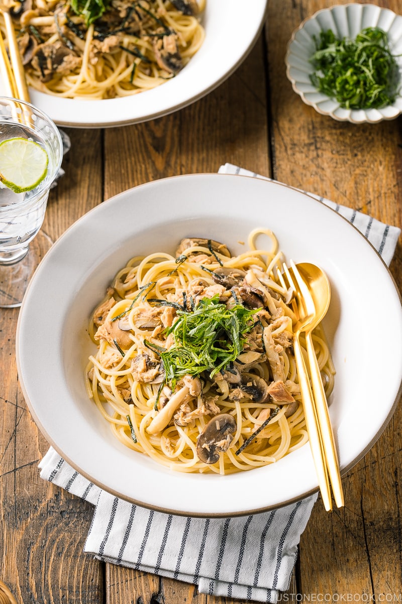 A white ceramic plate containing Japanese-style Tuna Mushroom Pasta garnished with shredded nori and shiso leaves.